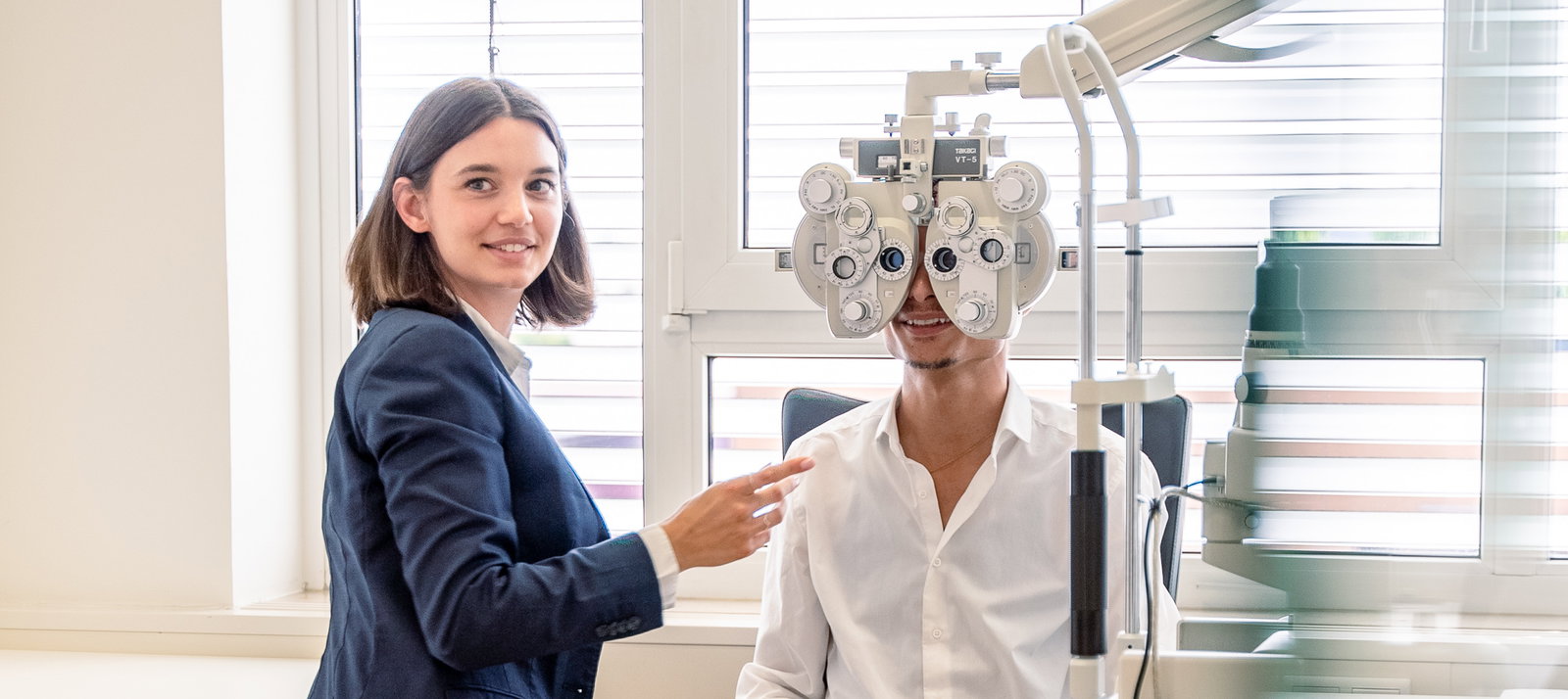 Das Bild zeigt eine Mitarbeiterin, die einen Sehtest mit einem Kunden macht.
